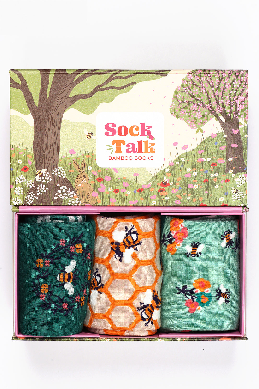 an artistic gift box designed to look like a summer meadow with wild flowers, cherry blossom trees and rolling hills with three pairs of ladies bamboo socks featuring bees and flowers