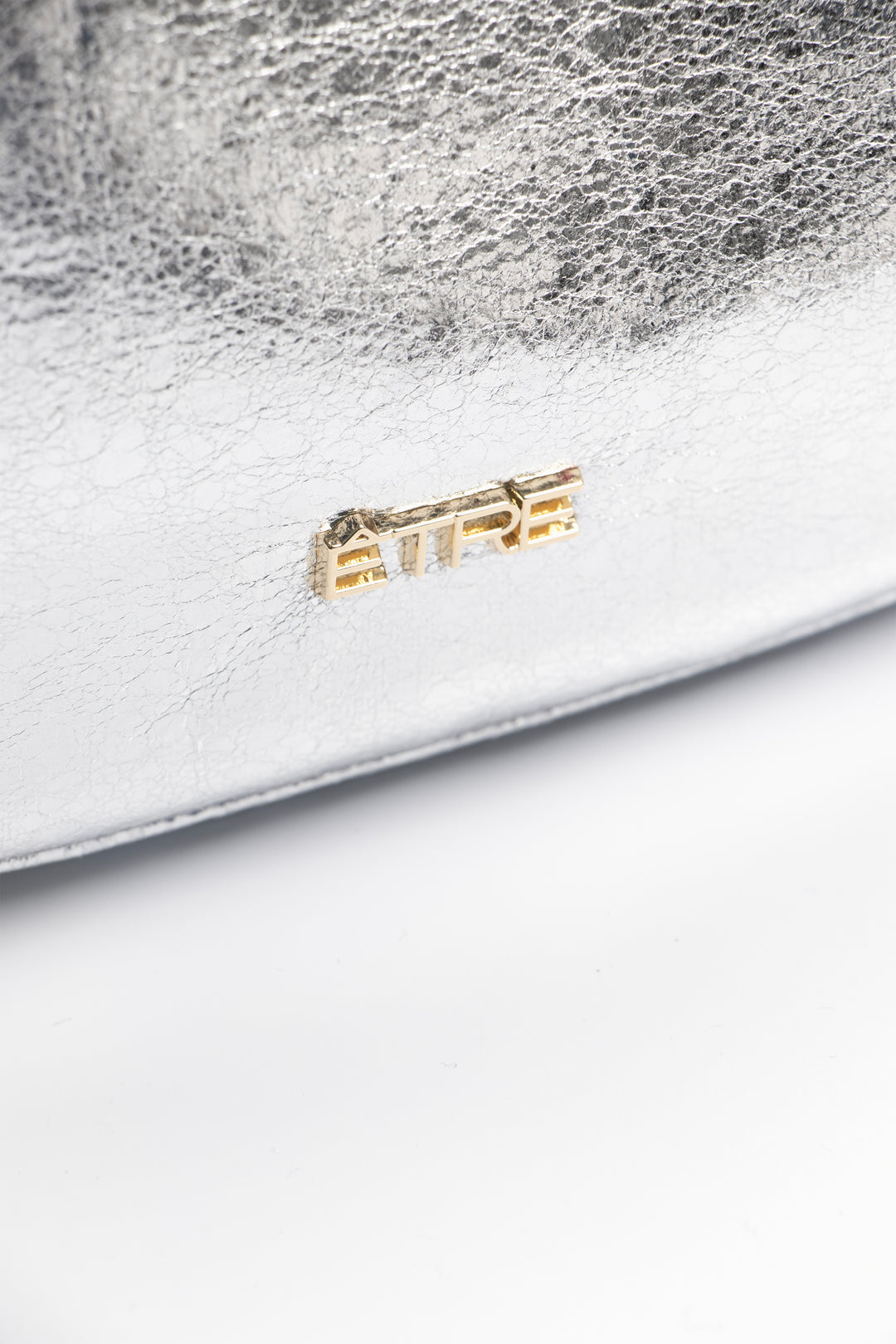 close up of the cracked faux leather and the gold etre logo on the front of the bag