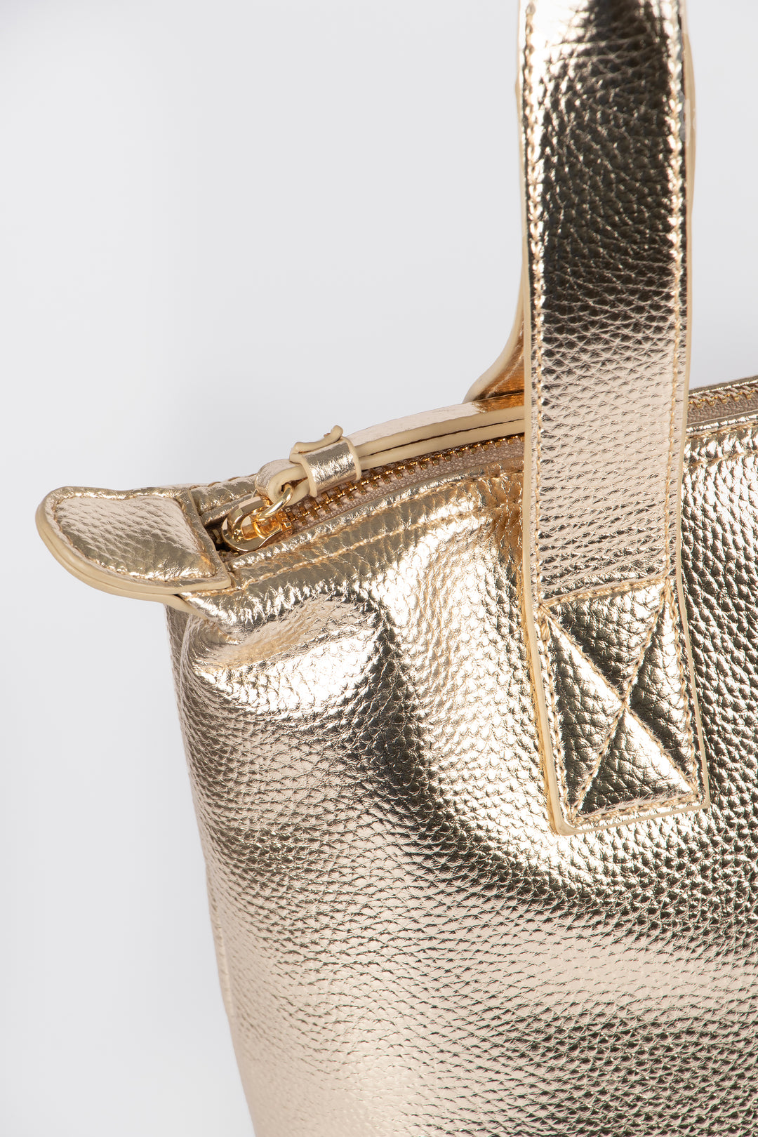close up of the top of the bag, showing clearly the gold zip closure main compartment and carry handles on the top.