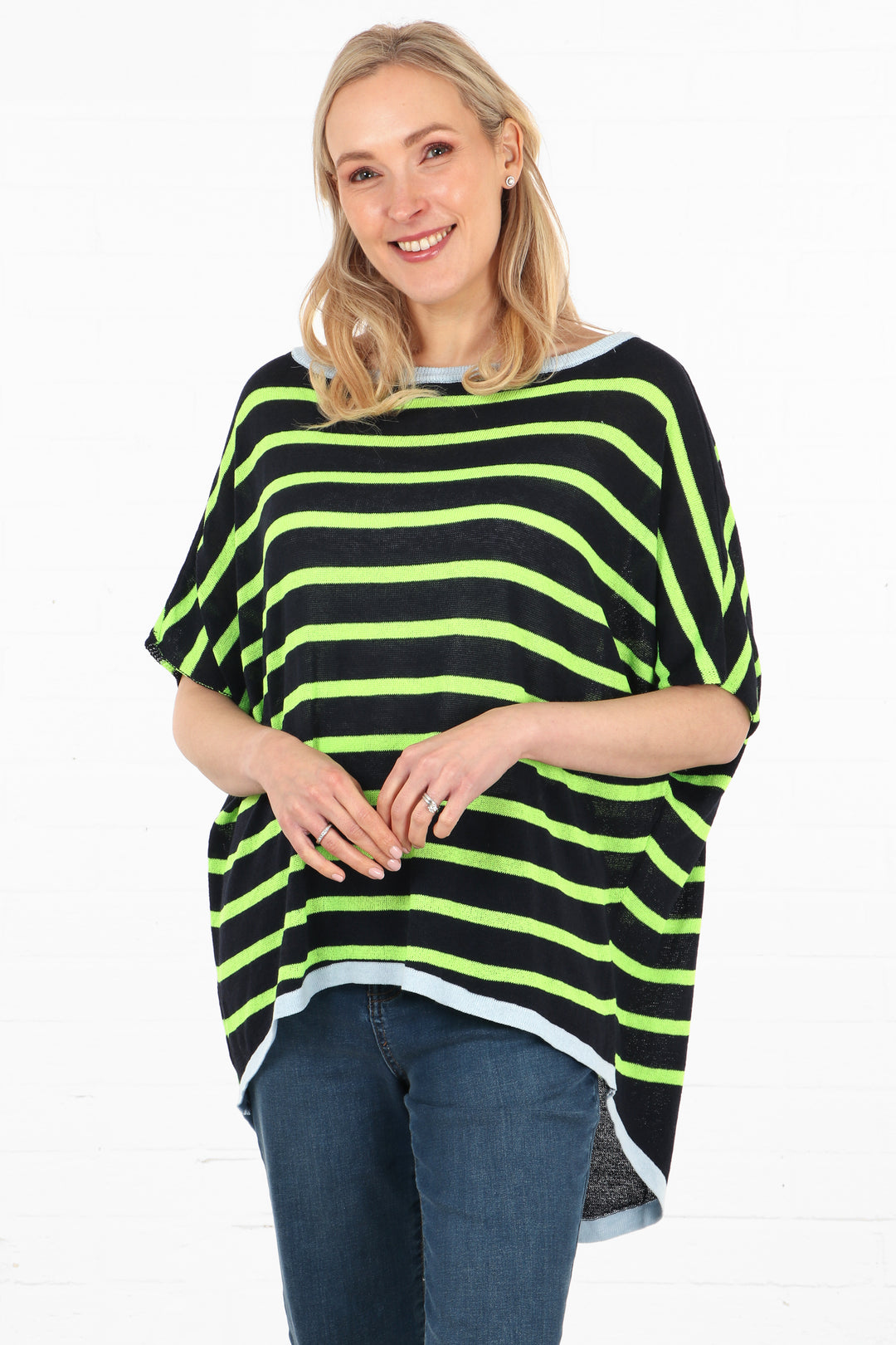 model wearing a navy blue and lime green stiped cotton jumper, the jumper has a dipped hem and short sleeves and a light blue trim around the neck and hem