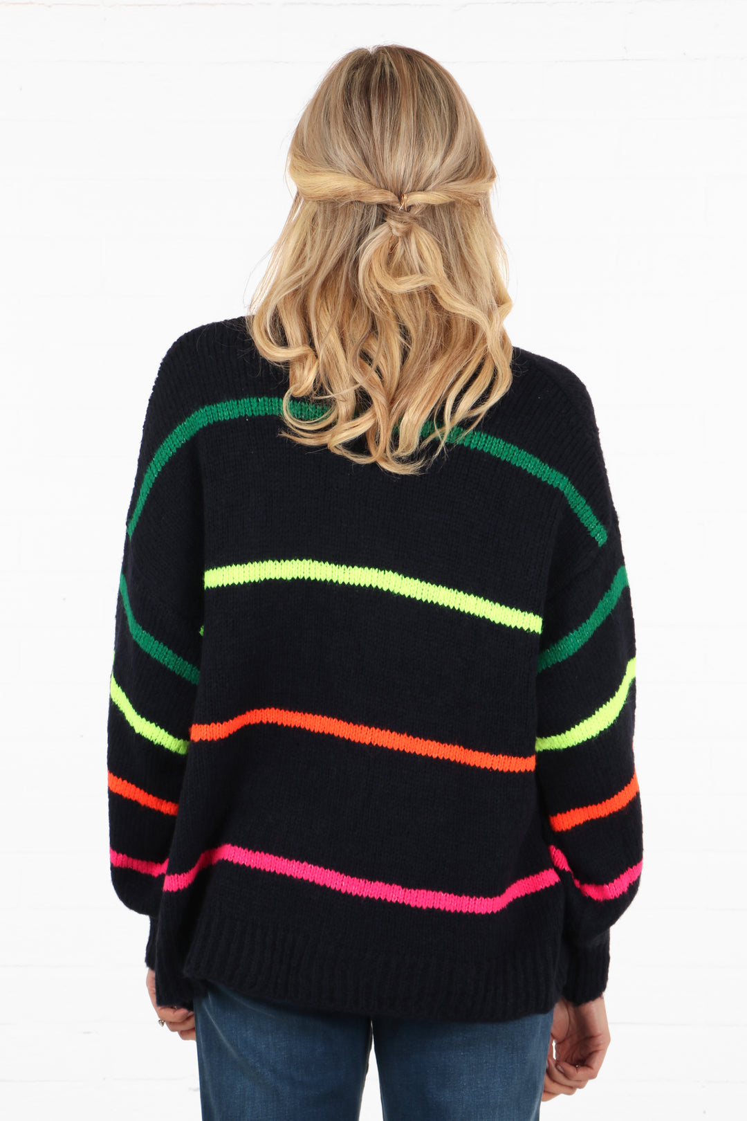 model showing the back of the navy blue knitted cardigan, showing that the multicoloured stripes are also on the back of the knitwear