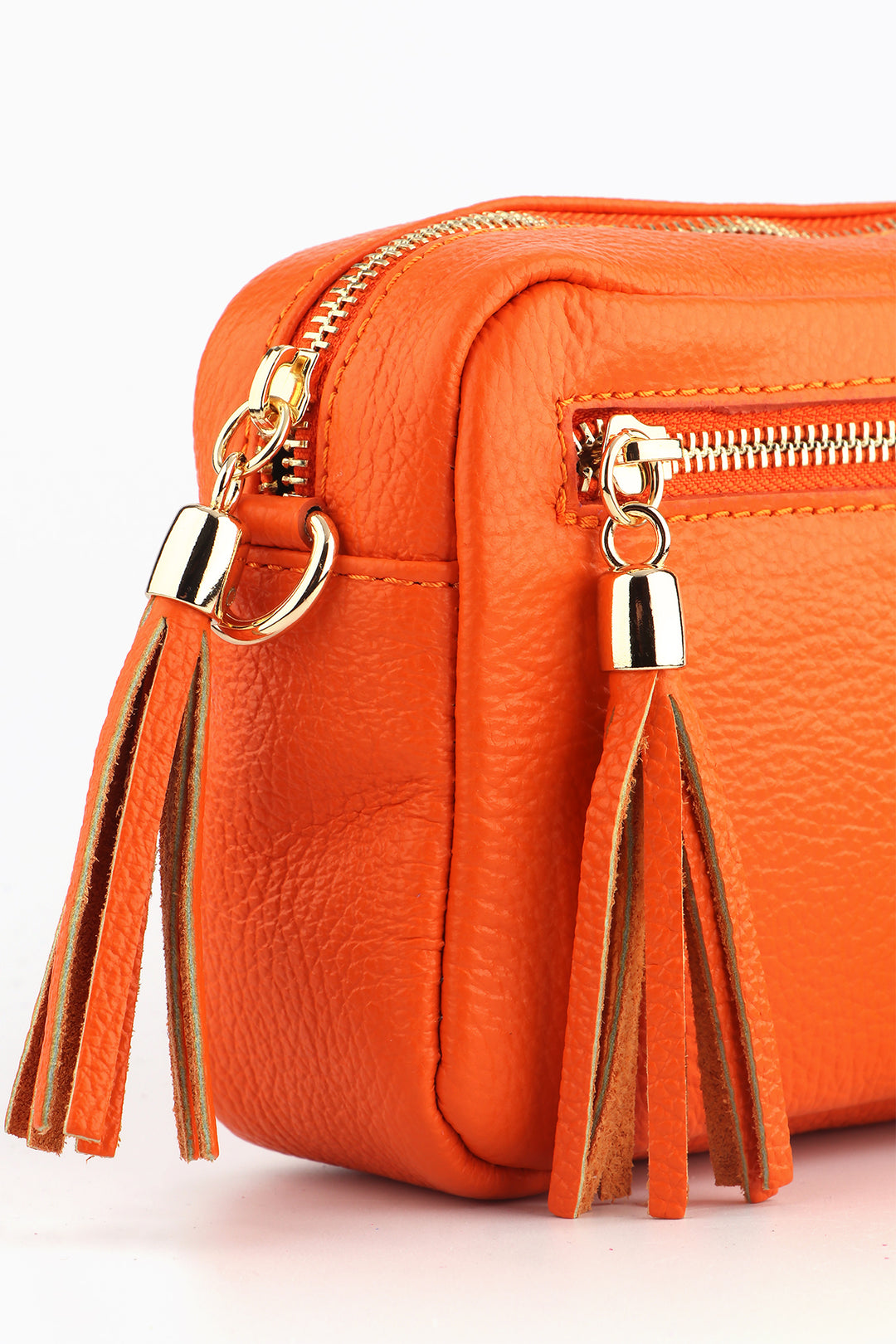 close up of the gold zip closure and tassel trim on the orange leather camera bag