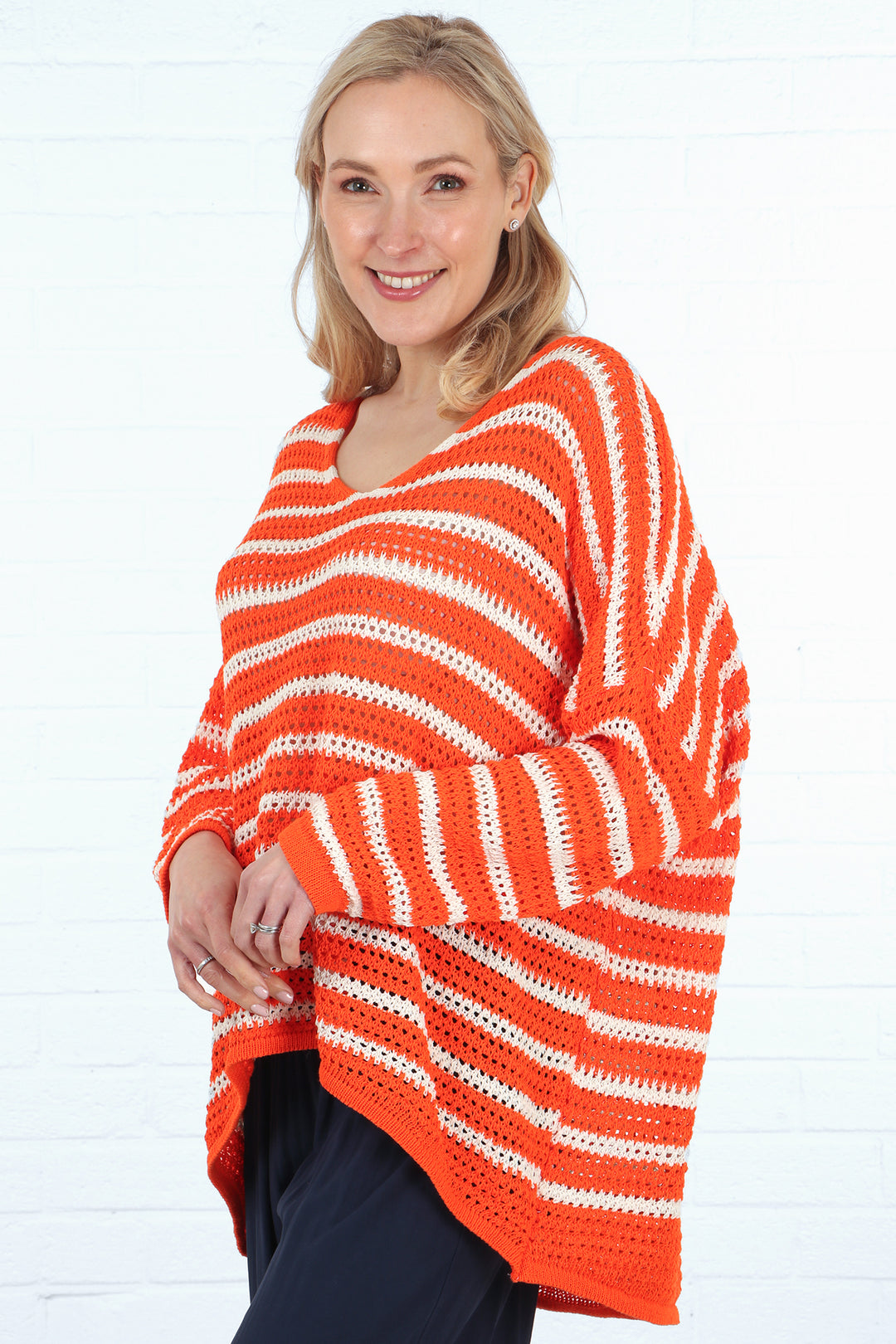 model wearing an orange and cream striped open knit cotton jumper, the jumper has a dip hem and long sleeves