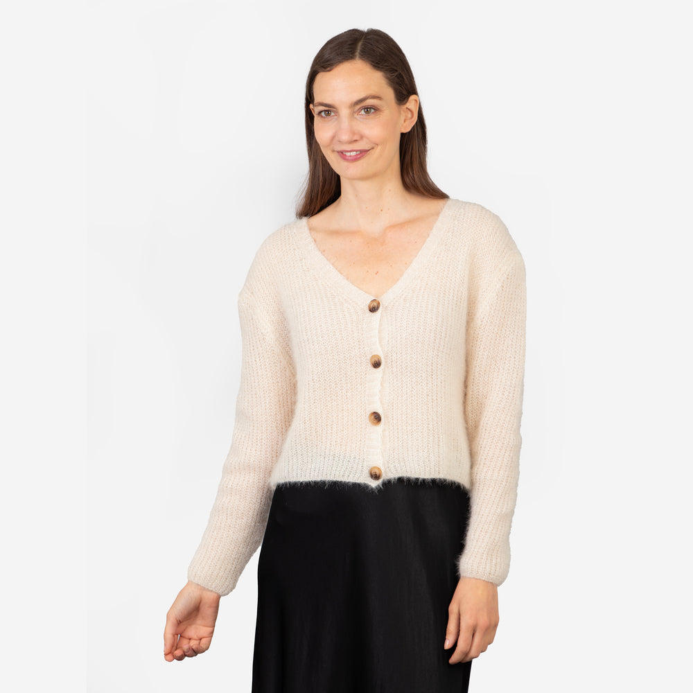 model wearing a cropped length beige knitted cardigan with a button up front