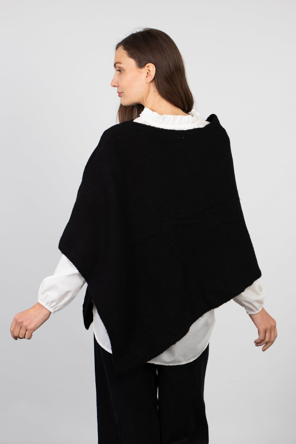 model showing the back of the black poncho, showing the asymmetrical hemline and loose fitting design of the piece