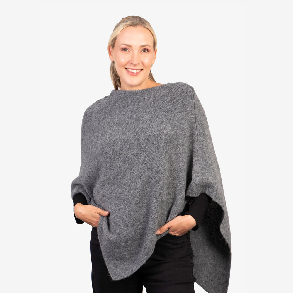 model wearing a grey knitted asymmetrical poncho with a cowl neck