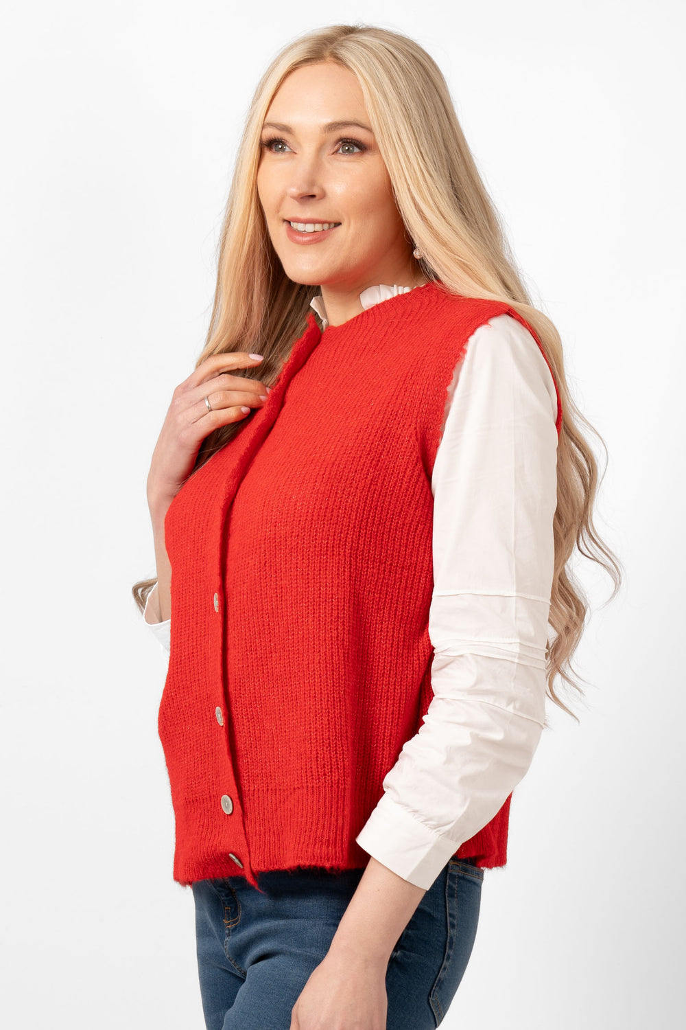 sleeveless red knitted tank top shown styled over a white blouse and paired with blue jeans.