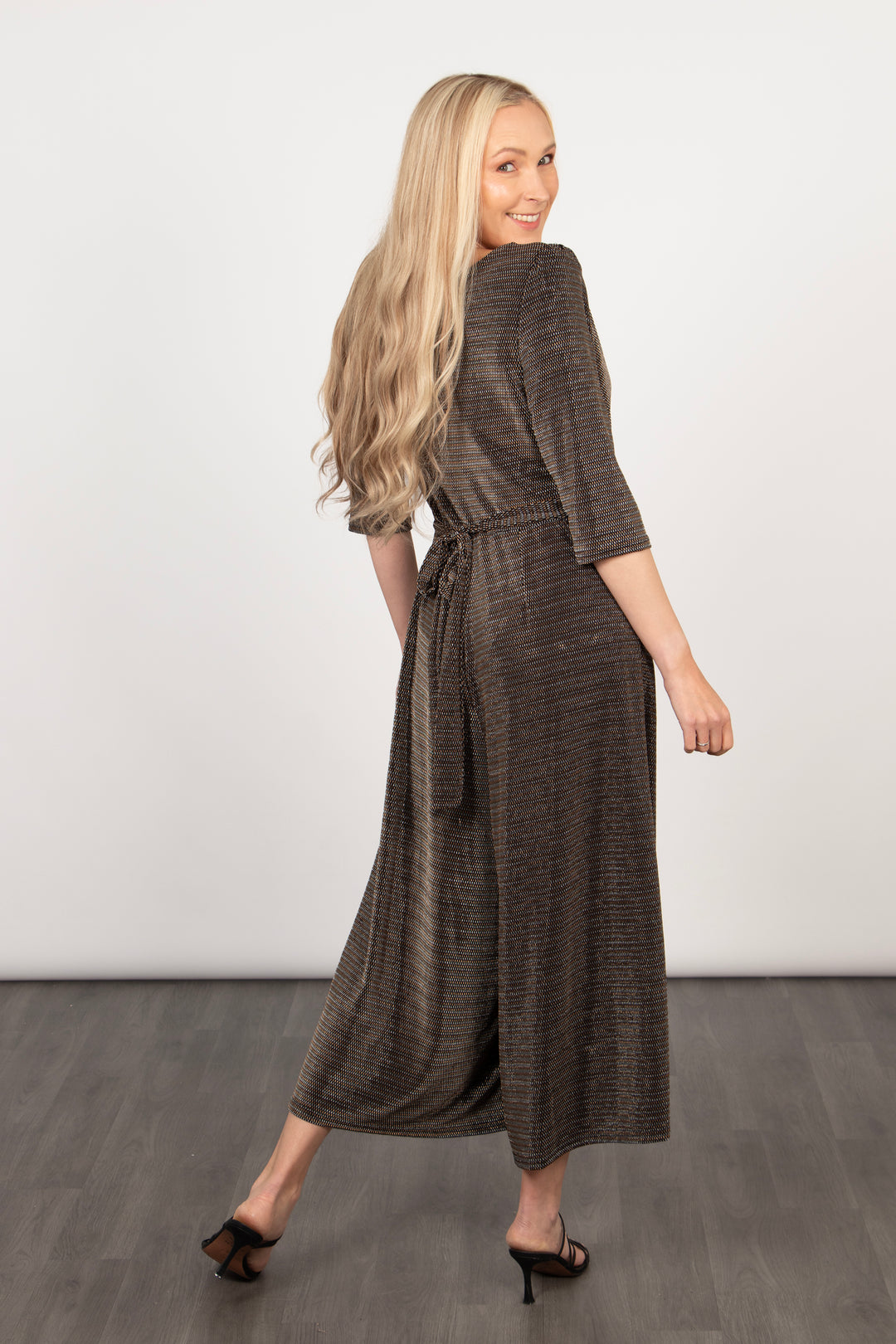 model showing the back of the black and gold glitter jumpsuit showing the waist tie feature at the back