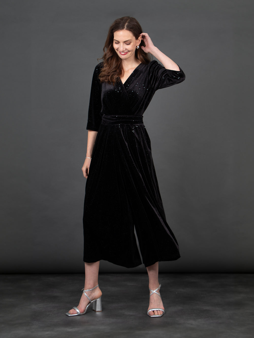 model wearing a cropped black velvet jumpsuit, the jumpsuit has an all over silver sparkle, v-neck and tie waist