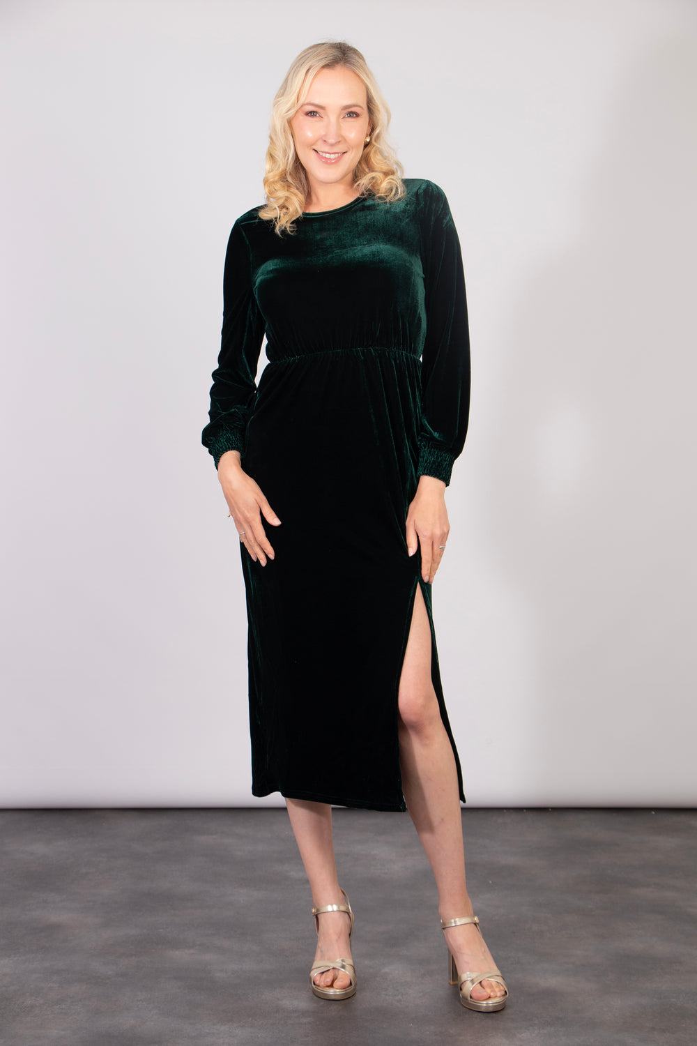 model wearing a green velvet midi dress with a thigh high side split, long sleeves and a round neck