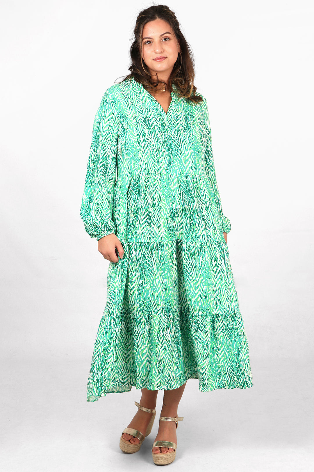 model wearing a midi length tiered dress with long sleeves and an all over green painted chevron print pattern
