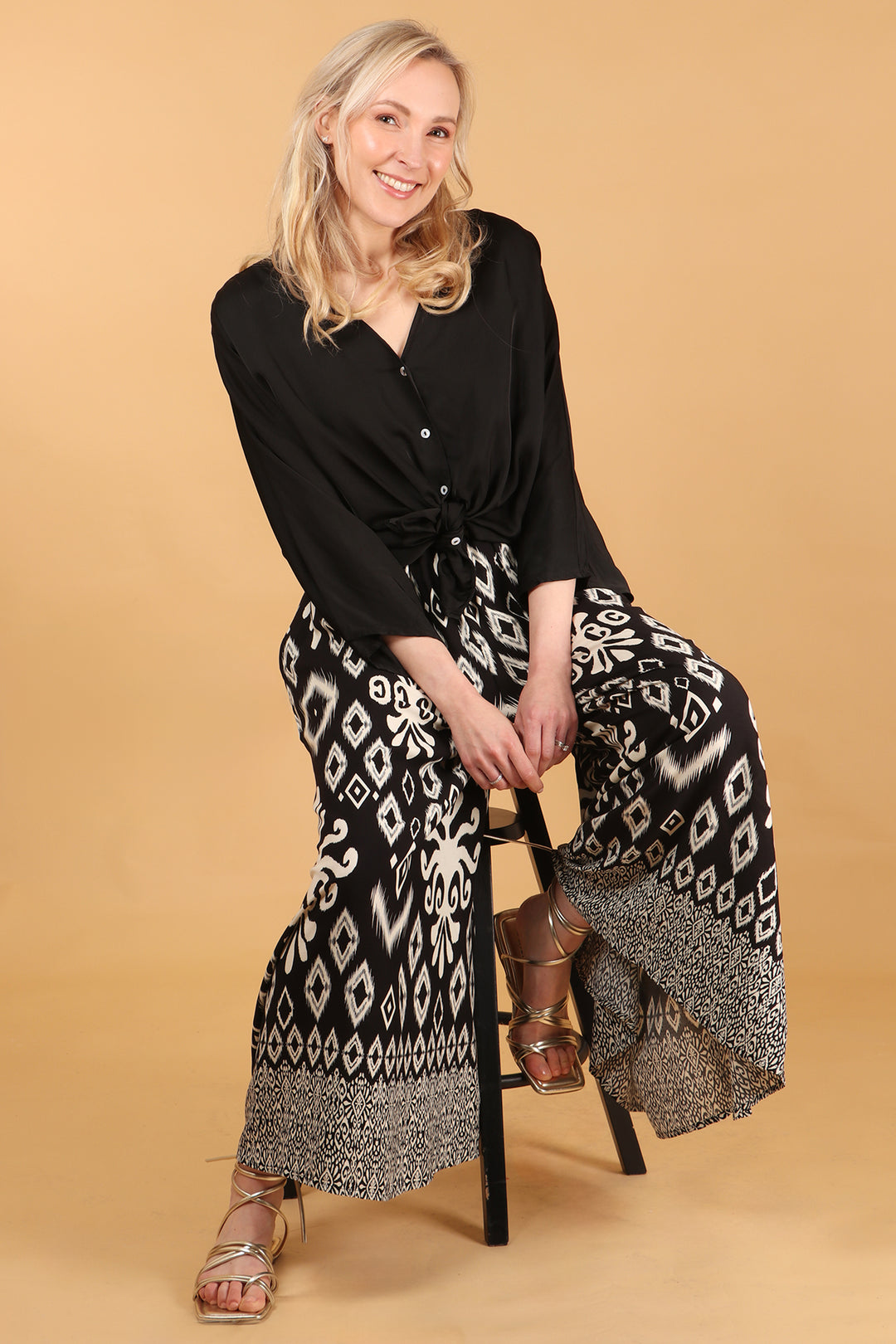 model wearing a pair of black wide leg palazzo trousers with a white ornate ikat pattern