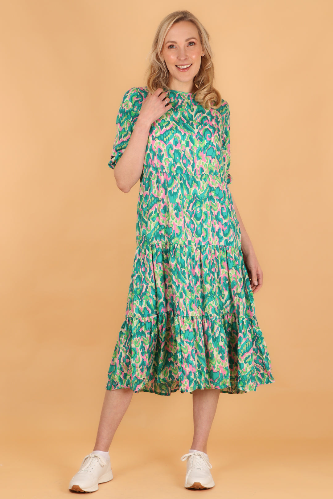 model wearing a midi length tiered dress with 3/4 sleeves with an all over green and pink abstract print pattern