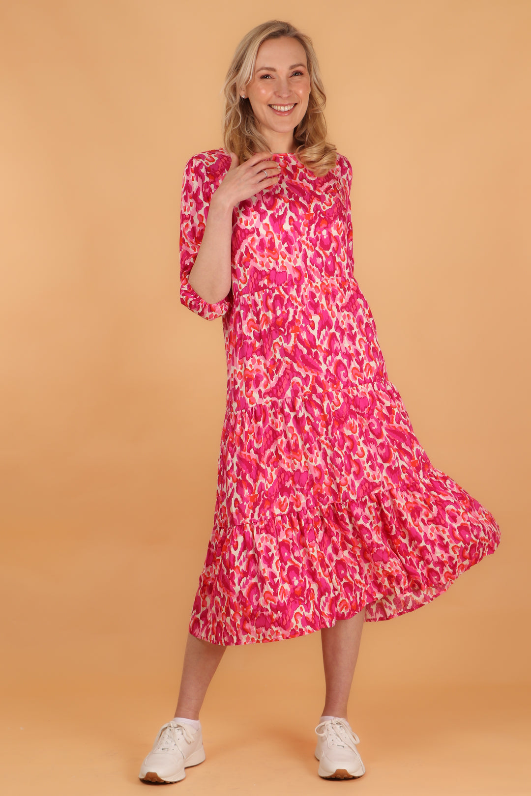 model wearing a midi length tiered dress with 3/4 sleeves with an all over pink abstract print pattern