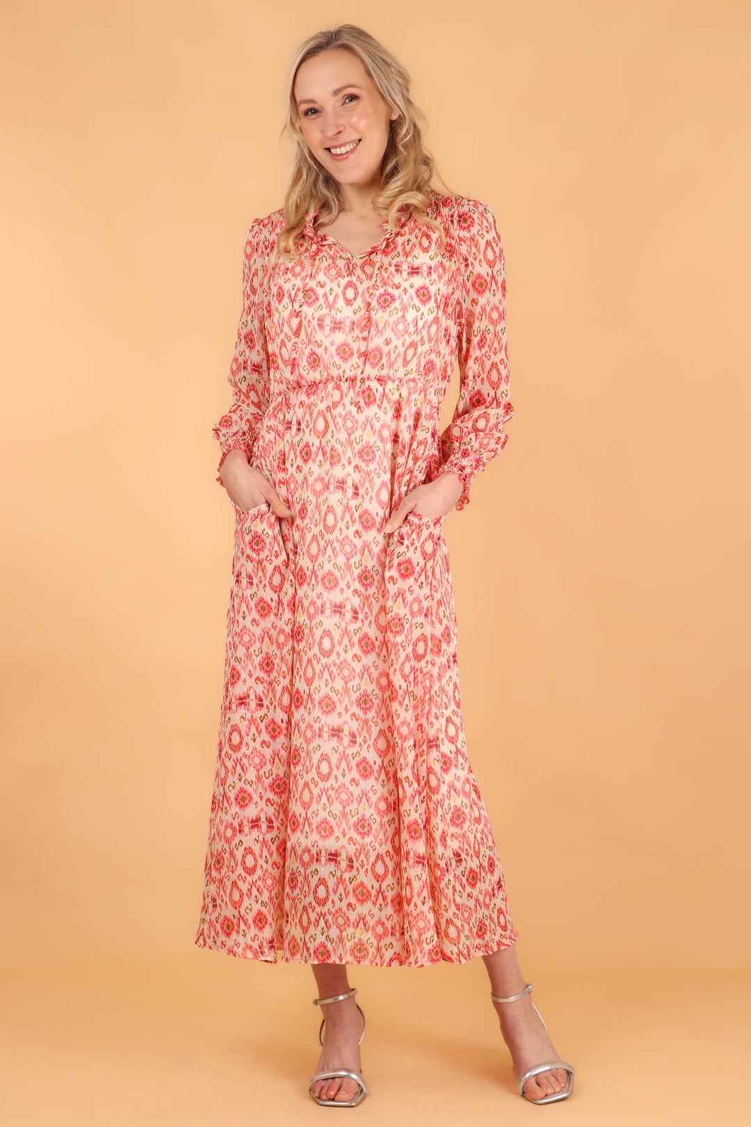 model wearing a midaxi length coral aztec print long sleeve dress, the dress has pockets