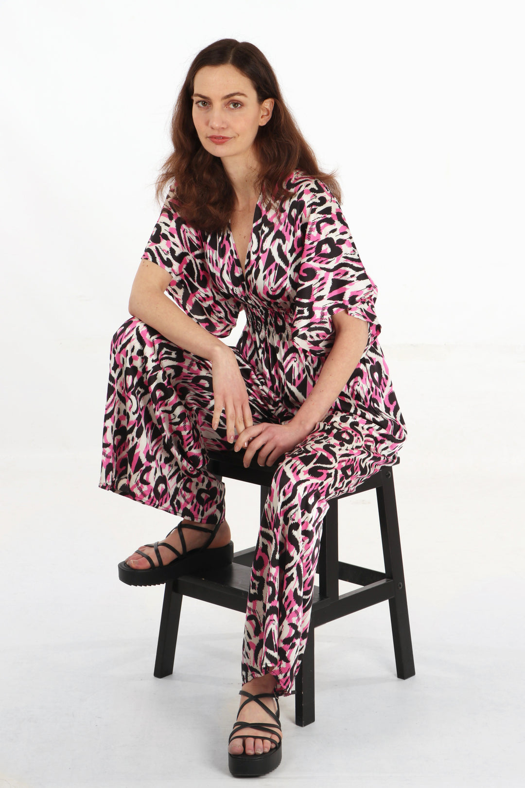 model seated wearing a pink abstract pattern jumpsuit with long flared trouser legs