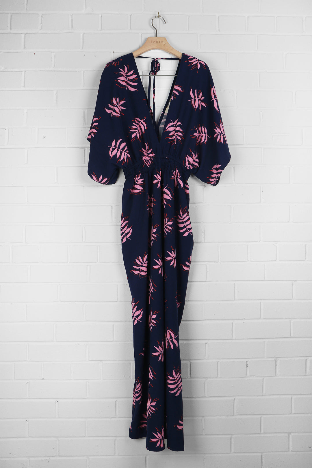 navy blue and pink leaf print jumpsuit draped on a coat hanger, the rear neck tie feature is clearly visible as is the shirred waist