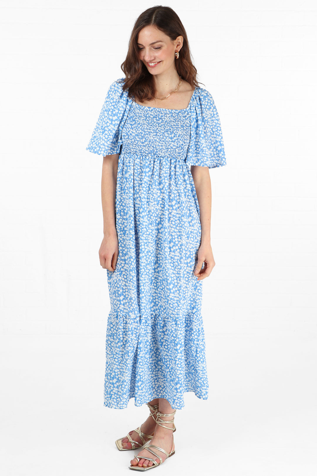 model wearing a blue and white ditsy floral pattern maxi milkmaid dress with short bell sleeves and a shirred bust