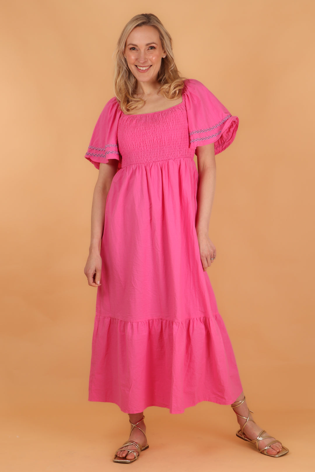 model wearing a pink maxi length tiered dress with a shirred bust and short bell sleeves