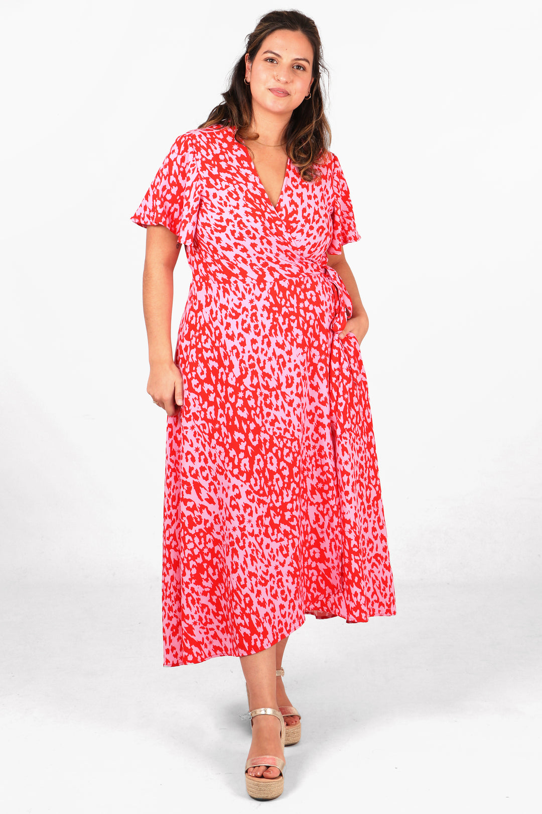 model wearing a midaxi length dip hem wrap dress with short angel sleeves and an all over pink leopard print pattern