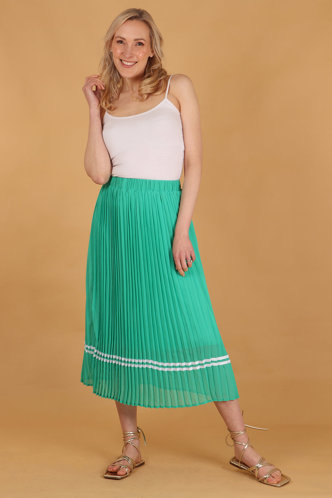 model wearing a green pleated midi skirt with two white stripes near the hem, the stripes are ribbon stripes