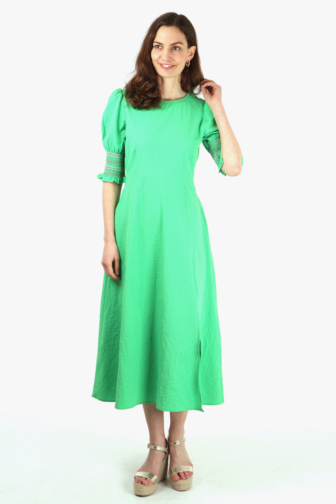 model wearing a green midaxi tea dress with embroidered shirred cuff sleeves, front split and round neck