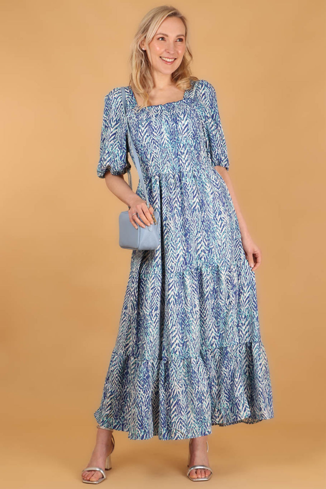 model wearing a blue chevron print square neck shirred maxi dress accessorised with a blue leather handbag