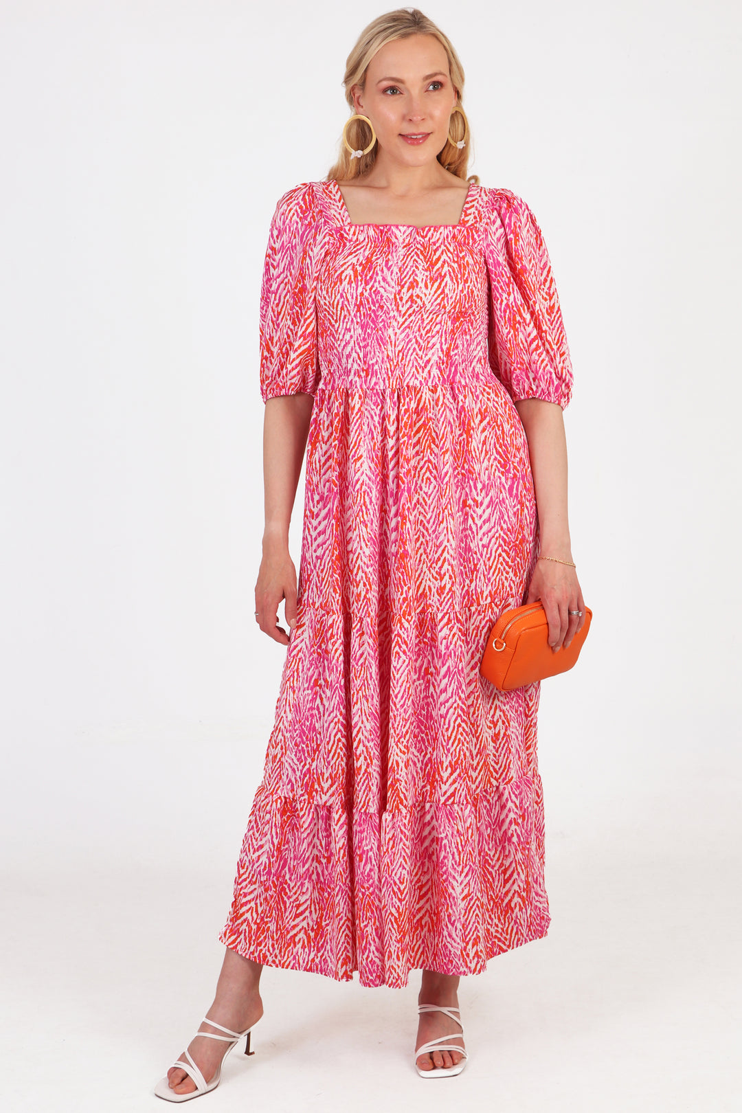 model wearing a pink tiered milkmaid dress with a pink chevron print, the dress is accessorised with an orange leather bag