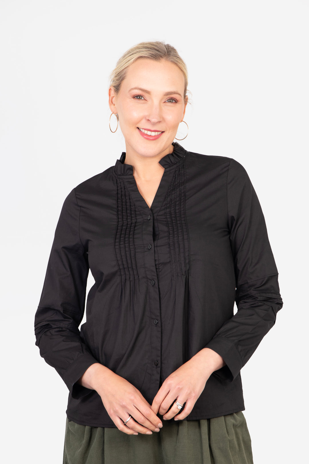 model wearing a black cotton shirt with button front closure. the shirt has long sleeves and a pleated front