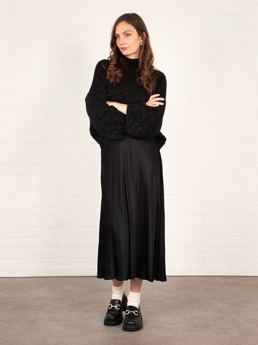 model wearing a plain black silky midi slip skirt, accessorised with a winter jumper and black shoes.