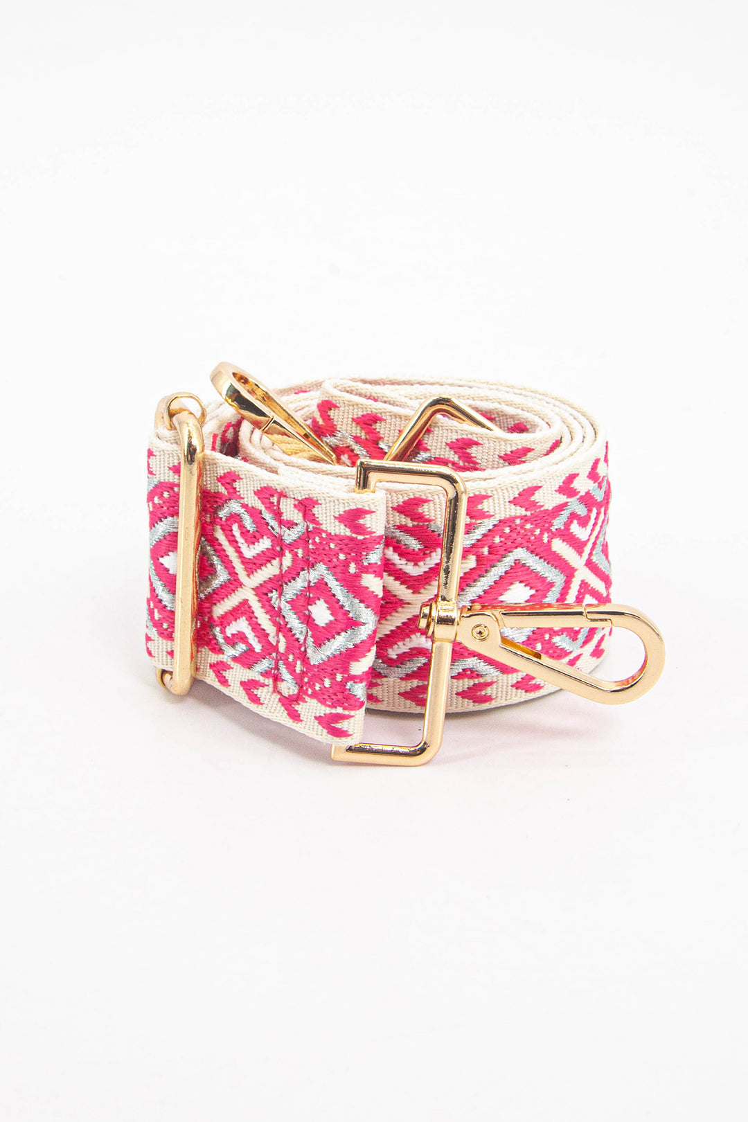 showing the bag strap coiled around itself, laying flat. the pink and silver geometric pattern is clearly visible as is the gold clip on hardware.
