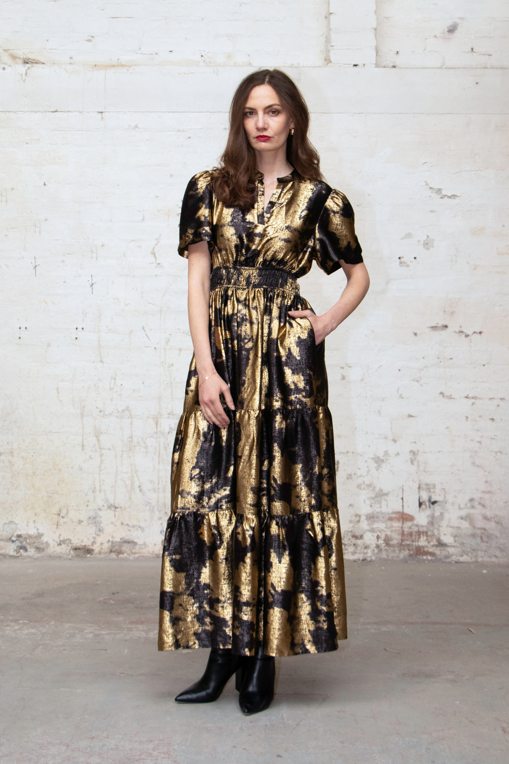 model wearing a short sleeve black and gold tiered maxi dress with a metallic sheen all over. the dress has a cinched elasticated waist