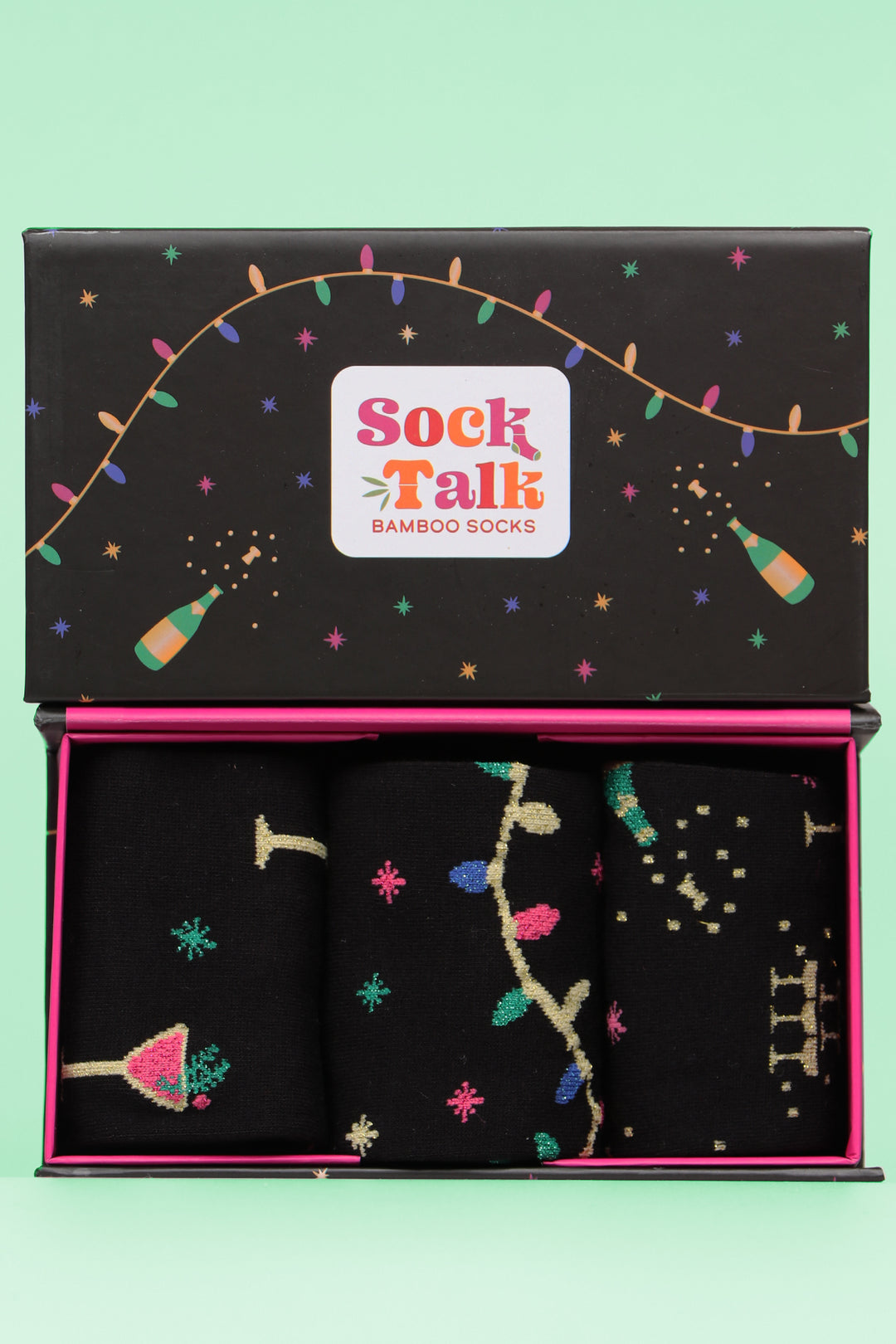 black gift box with a multicoloured pattern of champagne bottles, stars and party lights with three pairs of party themed bamboo glitter socks