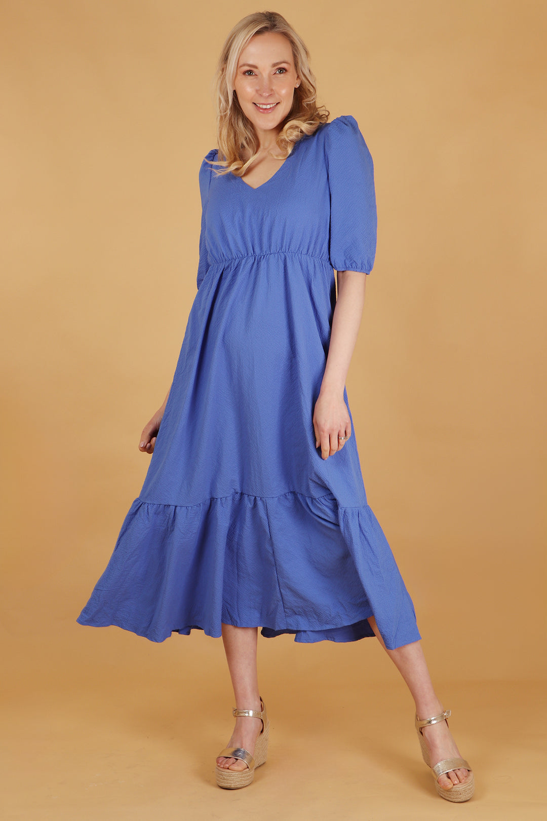 model wearing a plain blue textured midaxi length tiered dress with a vneck and short sleeves