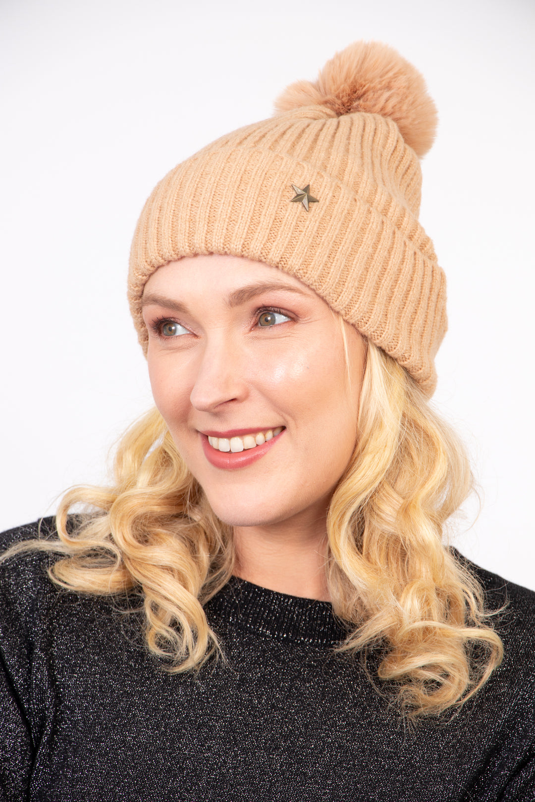 model wearing a camel coloured knitted ribbed beanie hat with a pom pom on top and a gold metallic star on the brim.