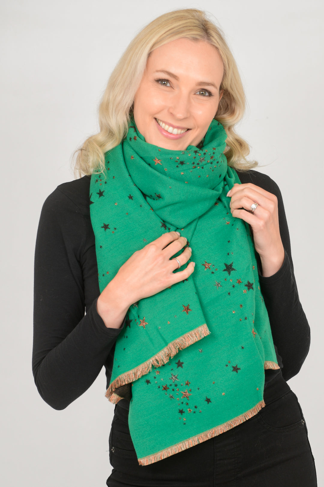 model wearing a green heavyweight winter scarf wrapped around the neck. the scarf is green with a scattered star print pattern with gold foil accents, the scarf also has a gold coloured fringed edge