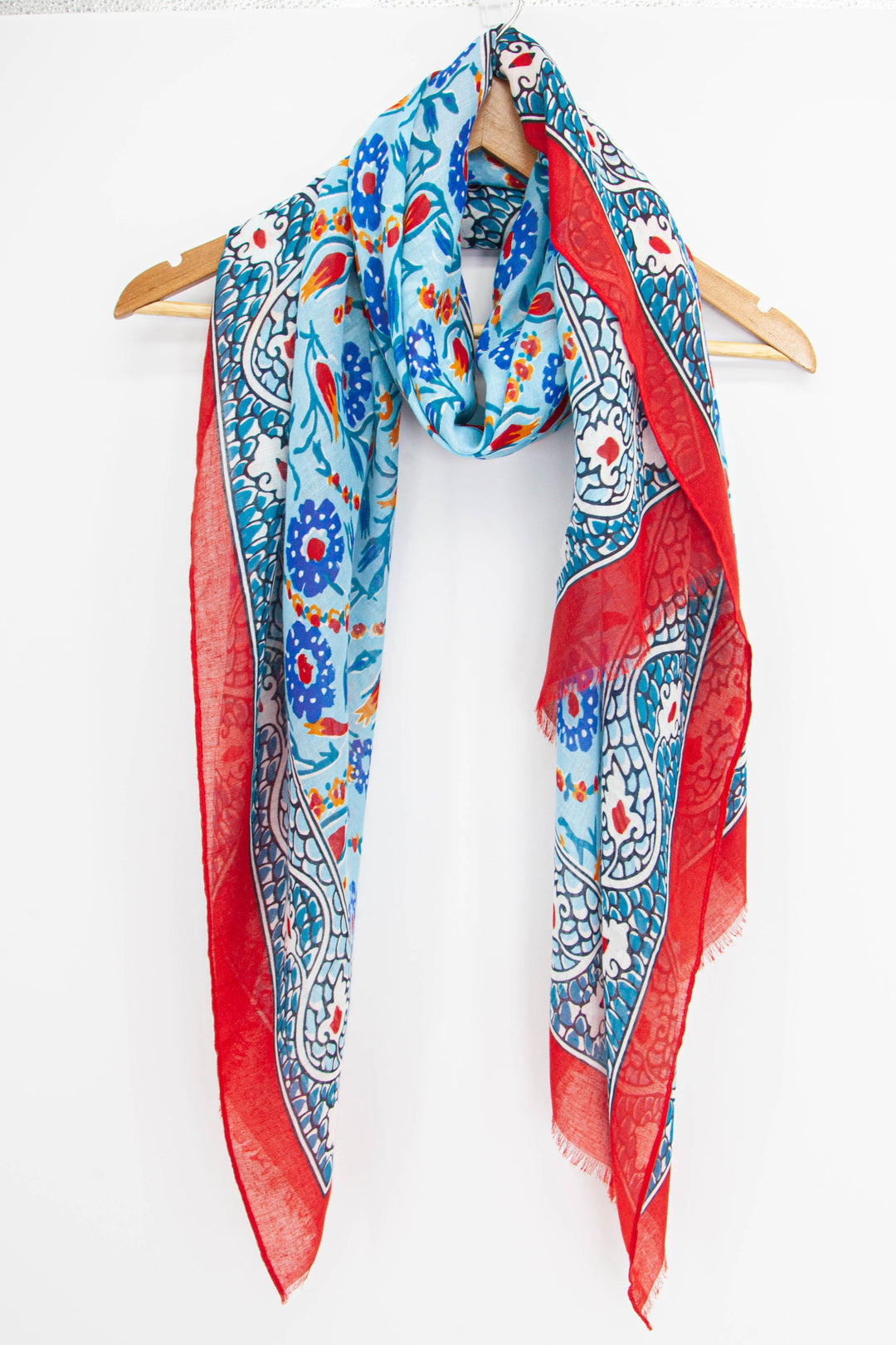 vintage paisley print scarf in blue draped around a coat hanger, showing the ornate pattern and contrasting red border trim