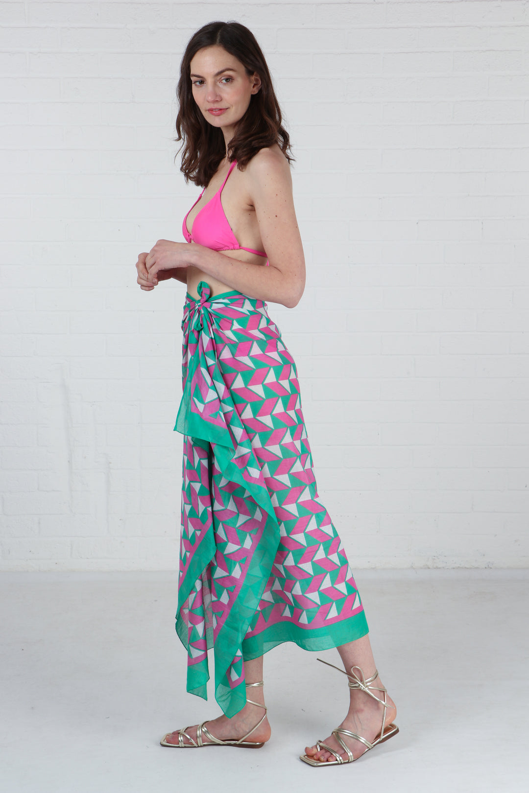 model wearing a pink and green geometric pattern scarf tied at the waist to show that it can be worn as a beach sarong