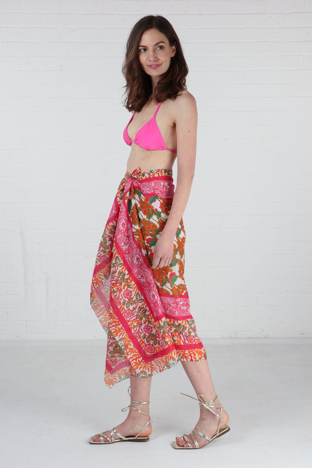 model wearing a pink and orange floral print scarf as a beach sarong