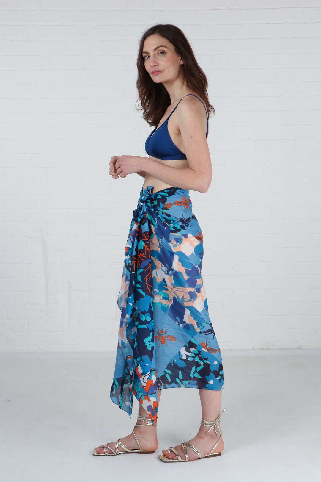 model wearing a blue floral bee print scarf tied around the waist to show it being worn as a beach cover up sarong