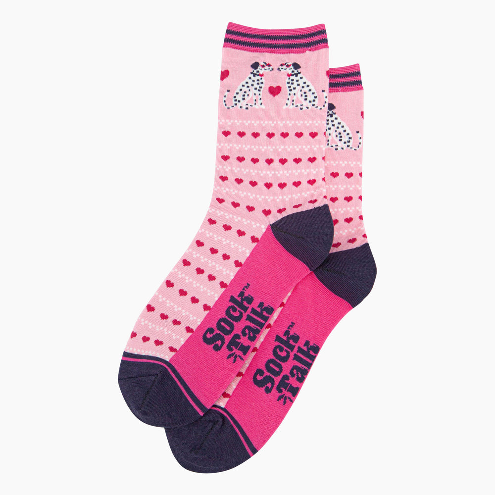 the pair of pink dalmatian dog socks laying flat, one overlapping the other. showing clearly the light pink background of the socks which is contrasted by the repeating rows of fuchsia pink love hearts. the dalmatians feature on the ankle of the socks. the sock talk logo is visible on the base of the sole. 