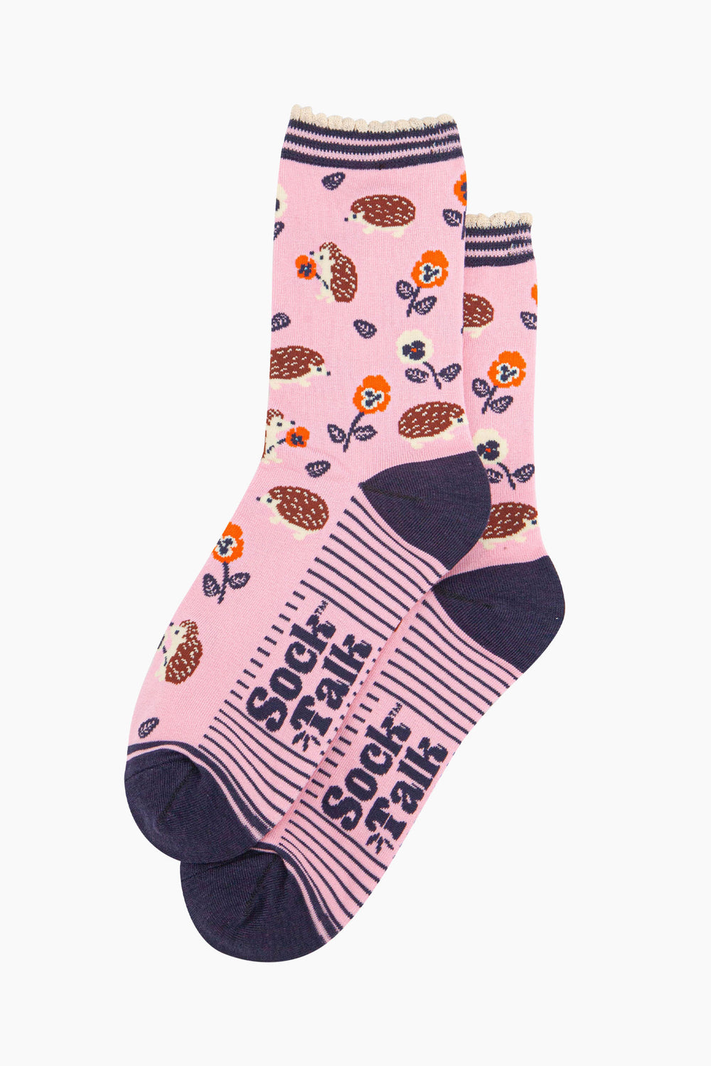 the pair of light pink hedgehog socks laying flat one overlapping the other. showing clearly the pink background of the socks which is contrasted by the all over pattern of hedgehogs, flowers and leaves.  the sock talk logo is navy blue and visible on the base of the sole. 