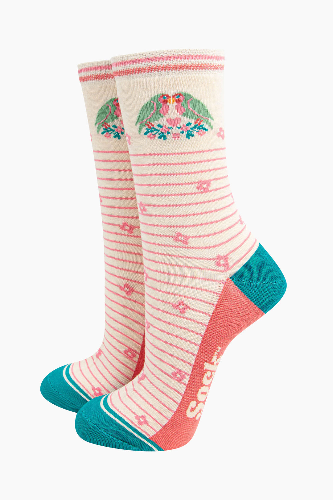 cream lovebird bamboo socks with a pink pinstripe pattern on the body of the socks. the heel and toe and aqua blue, the sole is coral pink. on the ankle of the socks there are a pair of green love birds perched on a floral branch.