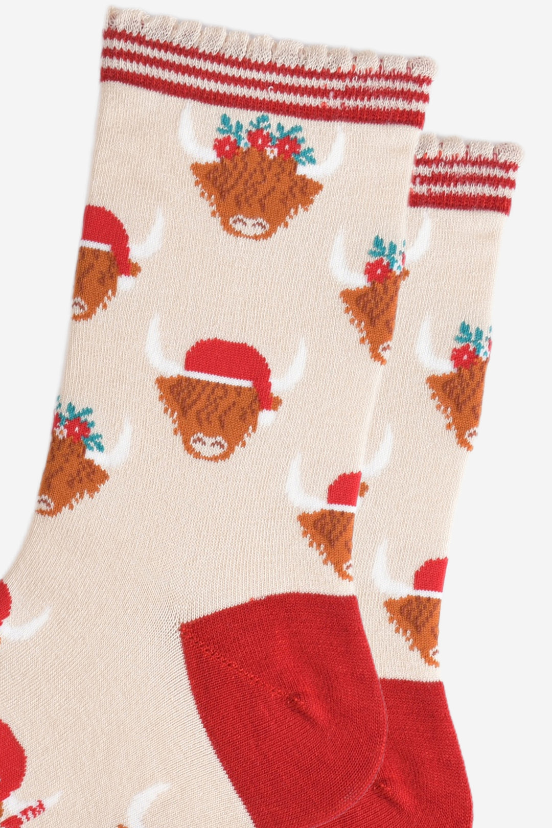 close up of the highland cow pattern on the socks, there are two designs, one with the cow wearing a red santa hat, the other the cow is wearing a festive green and red floral wreath as a crown