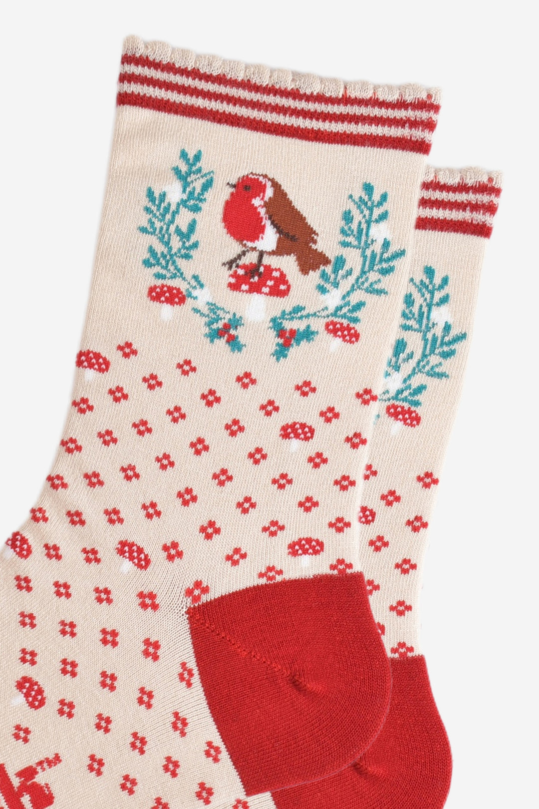 close up of the robin and wreath design on the ankle of the socks, the robin is sitting on top of a red toadstool and is positioned in the middle of the horseshoe shaped festive wreath. the wreath is green and features red holly berries and mistletoe