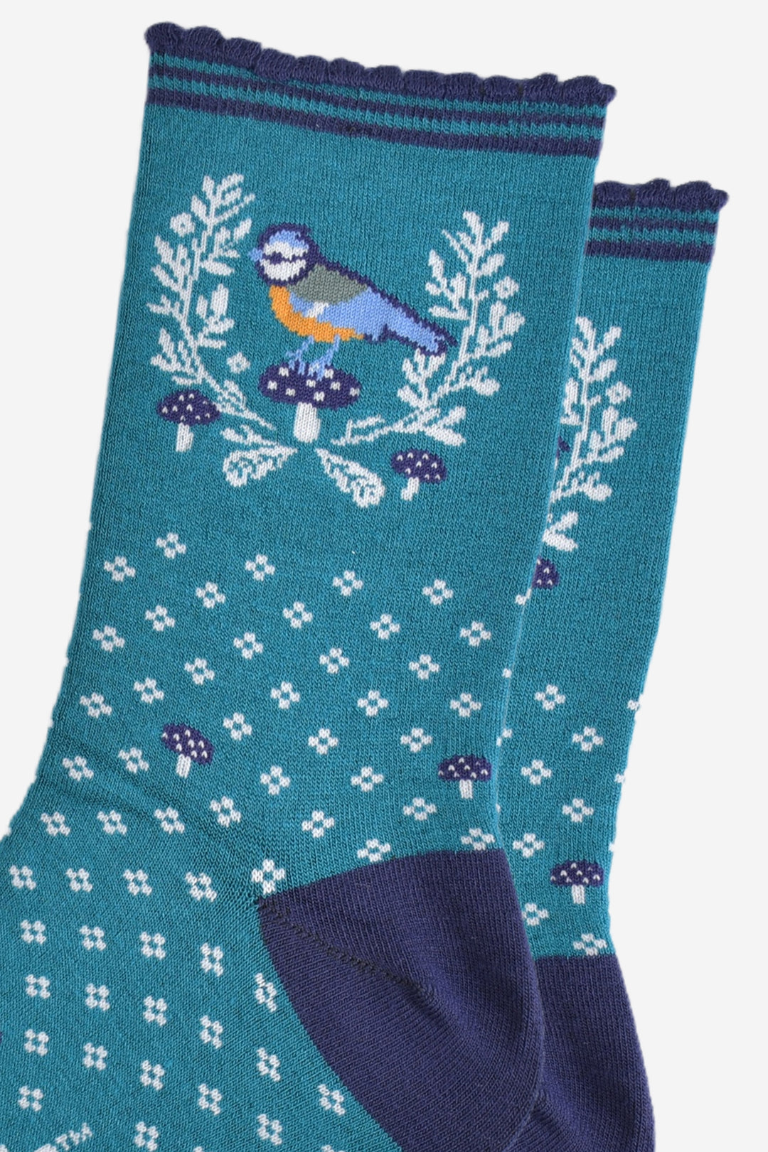 close up of the blue tit bird motif on the ankle of the socks, the bird is perched on a blue toadstool and surrounded by a white horseshoe shaped wreath