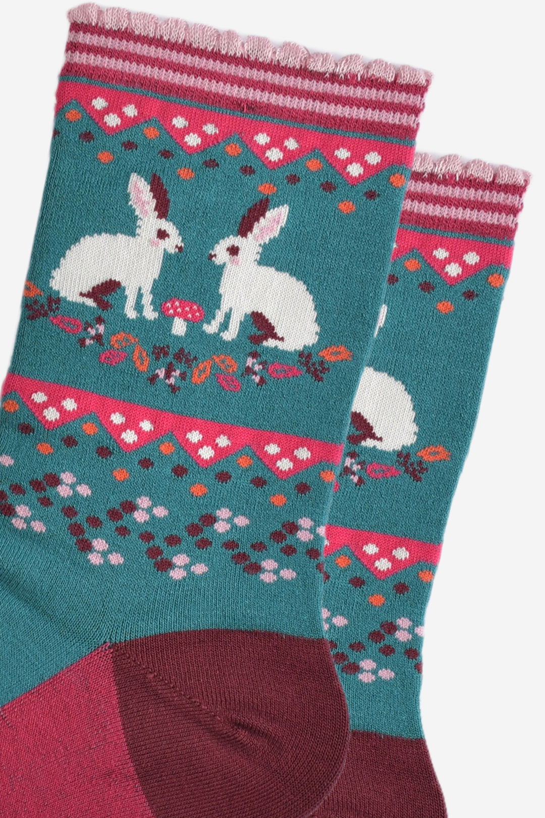 close up of the white rabbits on the ankle of the socks, there are two rabbits facing each other with a small pink toadstool inbetween, on the ground around the rabbits are fallen autumn leaves