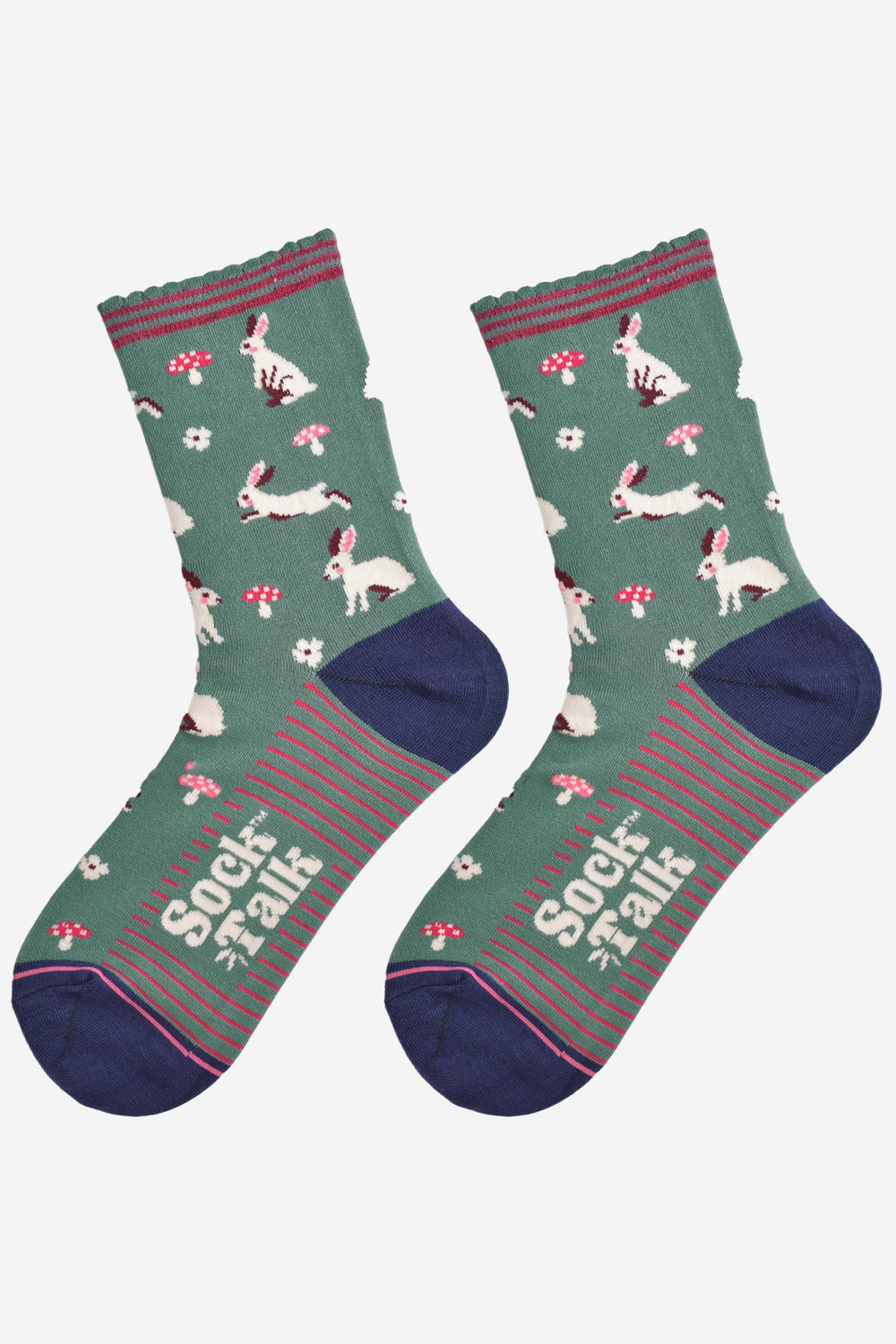 showing the woodland rabbit socks laying flat, there are white rabbits, hopping, sitting and standing among pink toadstools and white flowers, the solve of the socks has pink stripes in contrast to the green base of the design