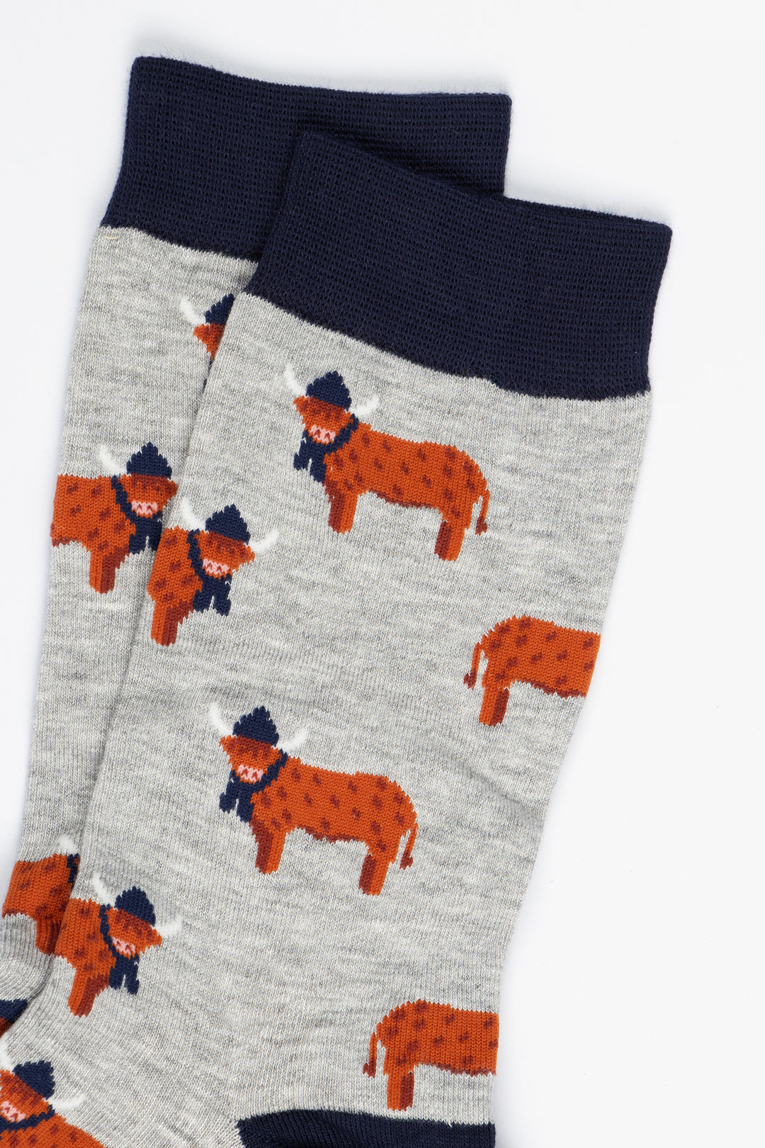 close up of the orange highland cows on the socks, the cows are standing up and they are designed to look like they have long hair, they are also wearing navy blue winter hats and scarves