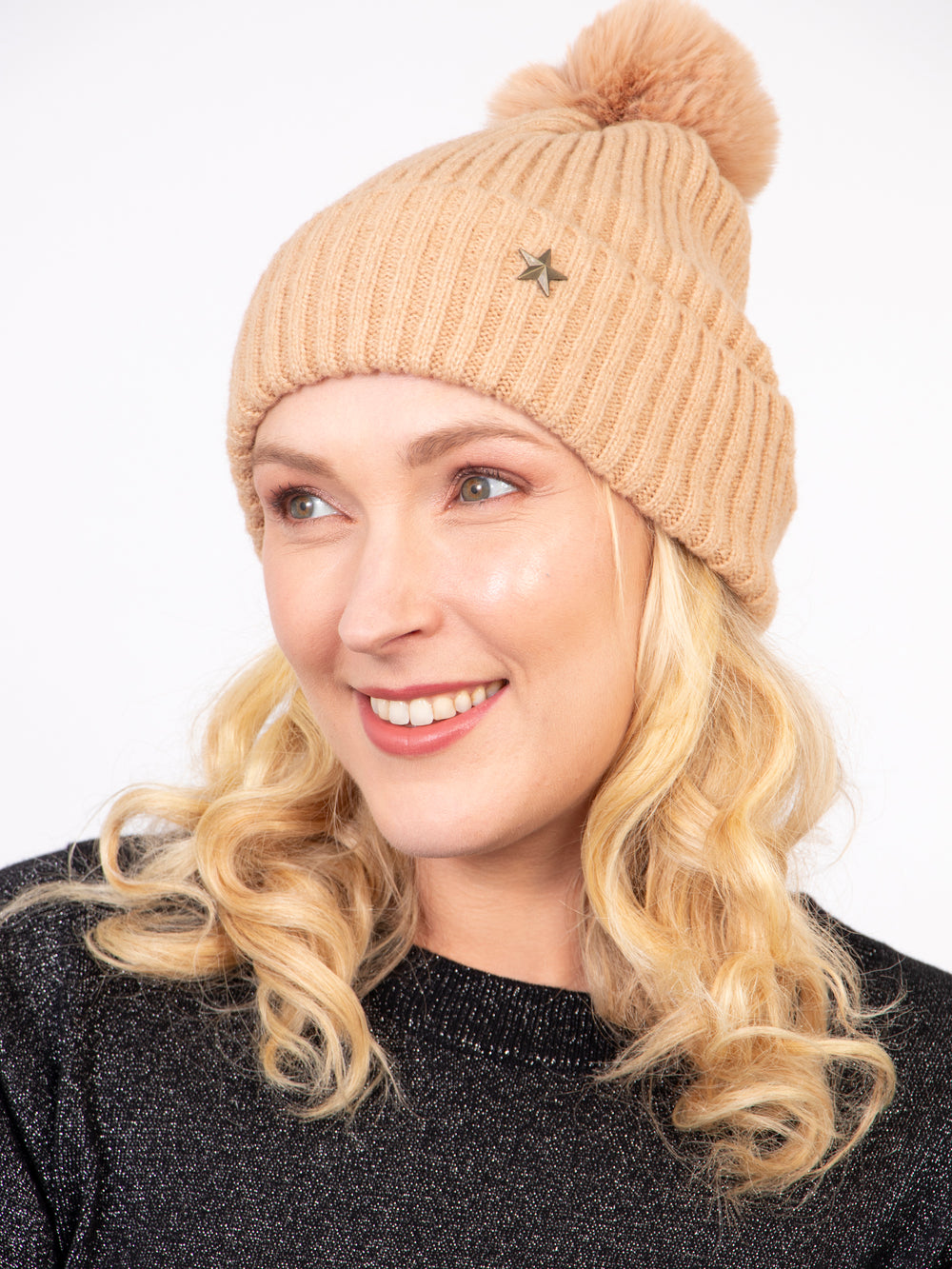 model wearing a camel coloured knitted ribbed beanie hat with a pom pom on top and a gold metallic star on the brim.